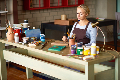 Portrait of beautiful young woman enjoying work in art studio painting picture on wooden base, copy space