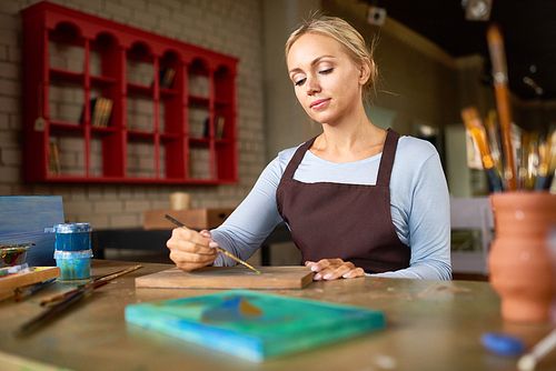Portrait of beautiful young woman enjoying work in art studio painting picture on wooden base making DIY decorations