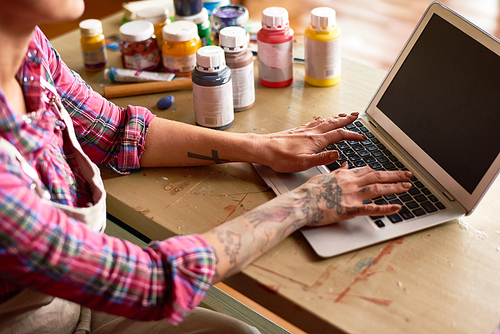 Close up view of creative young woman using modern laptop, focus on tattooed female hands typing