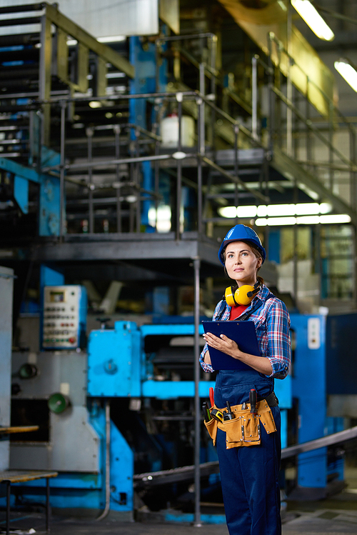 Portrait of female  worker working in modern plant looking up while  filling in papers on clipboard