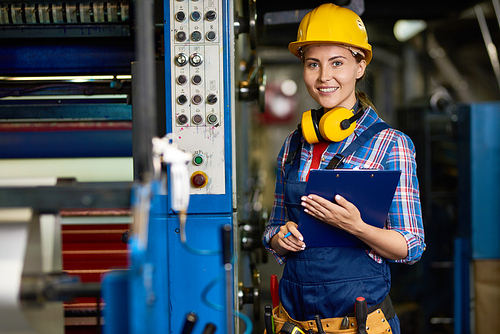 Portrait of cheerful young warehouse employee  with charming smile while doing checklist, she holding clipboard in hands