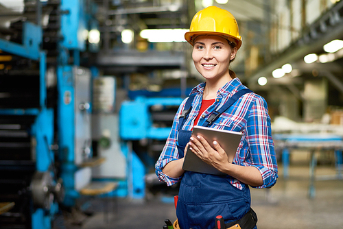 Portrait of beautiful young woman in hardhat smiling  at camera enjoying work in modern factory