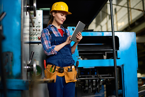 Portrait of female machine operator using digital tablet while working with power units in modern factory