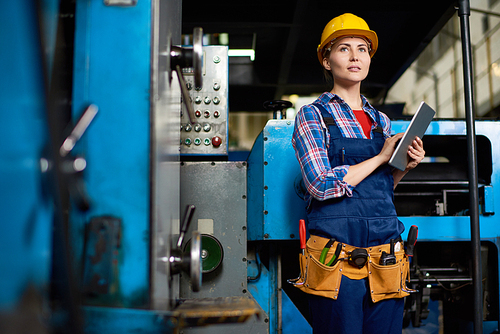 Talented young engineer wearing protective helmet holding digital tablet in hands while working at manufacturing plant