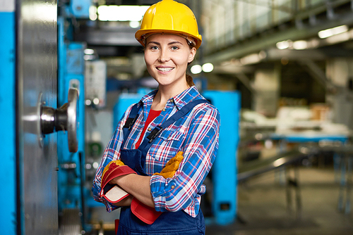 Portrait of beautiful young woman in hardhat smiling confidently at camera enjoying work in modern factory