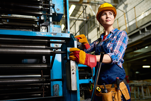 Portrait of female factory worker setting up machine units looking away confidently in modern plant