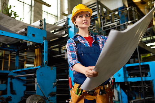 Portrait of female factory worker, young woman holding freshly printed pages looking away