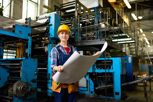 Portrait of female factory worker holding freshly printed pages looking away