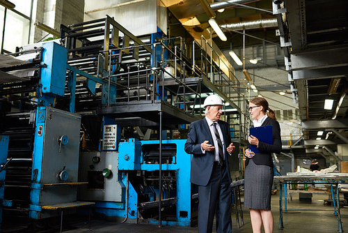Portrait of senior businessman wearing hardhat talking to assistant manager in modern factory workshop