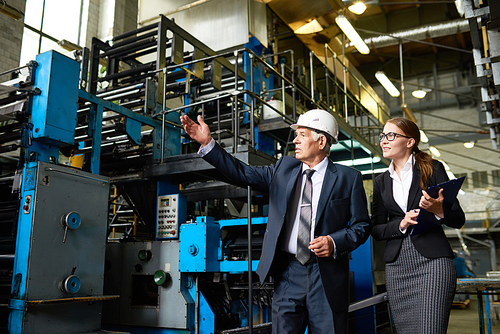 Portrait of senior businessman or executive manager wearing hardhat touring modern factory with young assistant