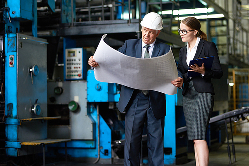 Portrait of senior businessman discussing floor plans of modern factory with young assistant manager in workshop