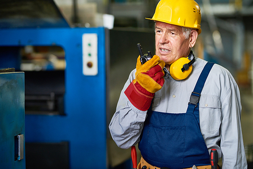 Portrait of senior factory worker using portable radio set  talking to somebody in workshop