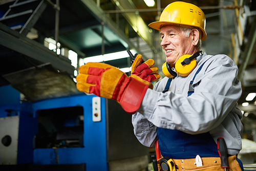 Portrait of senior factory worker using portable radio set and smiling talking to somebody in workshop