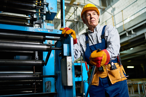 Low angle portrait of senior factory worker  standing by machine in modern industrial workshop