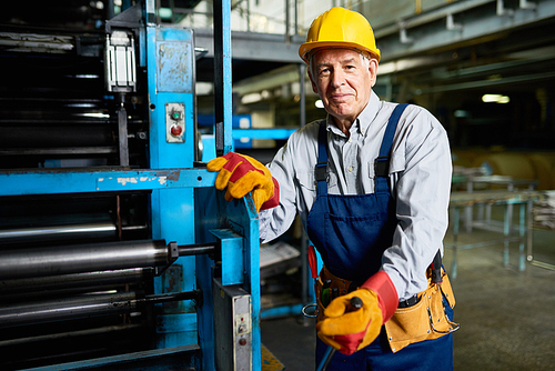 Portrait of senior factory worker smiling  standing by machine in modern industrial workshop