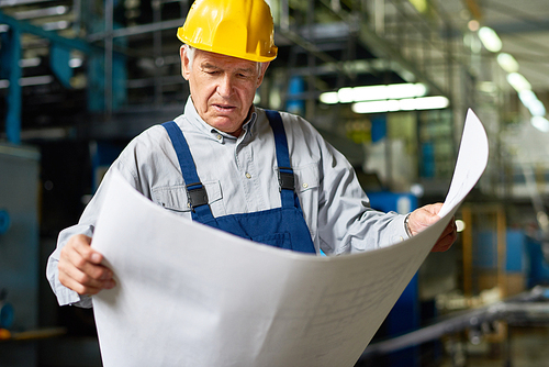 Portrait of senior man looking at floor plans in workshop of modern factory
