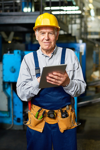 Portrait of senior factory worker using digital tablet and smiling at camera posing in modern workshop