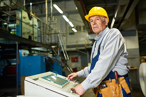 Portrait of senior man operating machine units in modern factory standing by control panel and looking away