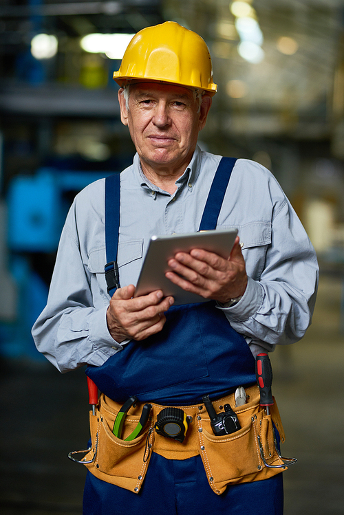 Portrait of senior factory worker using digital tablet and smiling at camera in modern workshop