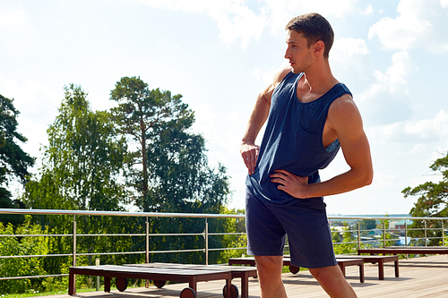 Portrait of handsome young man doing warm up exercises during workout outdoors in sunlight, copy space