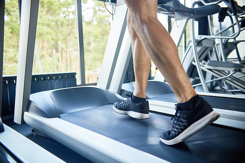 Close-up shot of unrecognizable sporty man running on treadmill in modern gym with panoramic windows