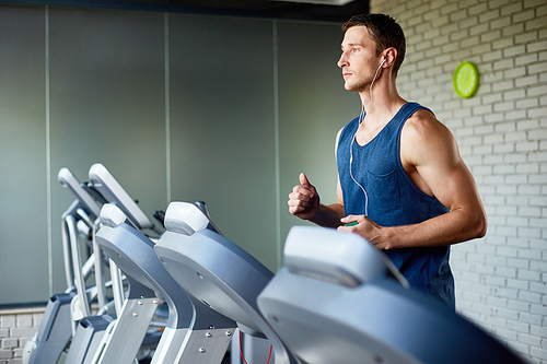 Portrait of muscular young man running on treadmill in modern gym during cardio workout, copy space