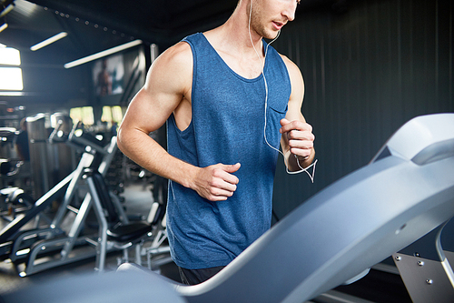 Mid section portrait of muscular young man running on treadmill in modern gym during cardio workout