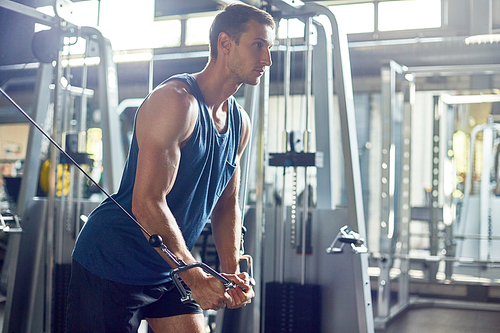 Side view portrait of handsome muscular man using exercising machines in modern gym, copy space