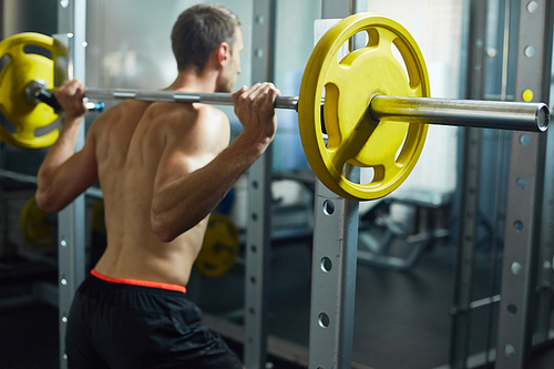 Rear view portrait of handsome muscular man with bare back lifting heavy barbell during workout in modern sports club, copy space