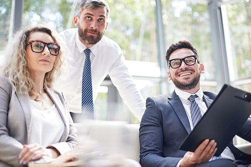 Talented group of managers in formalwear looking away with interest while having productive working meeting at modern boardroom, panoramic windows on background