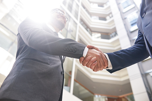 Low angle view of unrecognizable businessmen shaking hands after successful completion of negotiations, lens flare