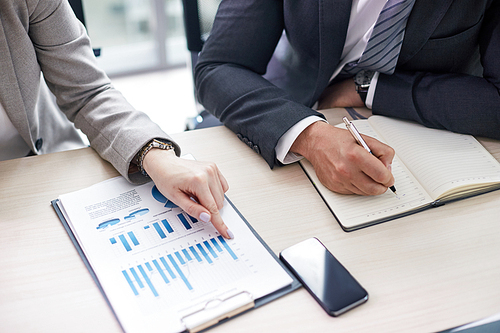 Close-up shot of unrecognizable colleagues studying financial figures while sitting at desk of modern open plan office