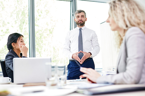 Portrait shot of confident bearded entrepreneur  while standing at marker board and making presentation to multi-ethnic group of colleagues, interior of boardroom on background