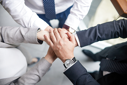 Group of colleagues in formalwear joining hands together while celebrating completion of joint project, close-up shot