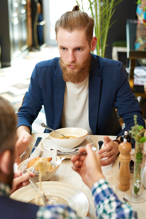 Over shoulder view of confident bearded entrepreneur conducting negotiations with business partner while having lunch at cozy small restaurant