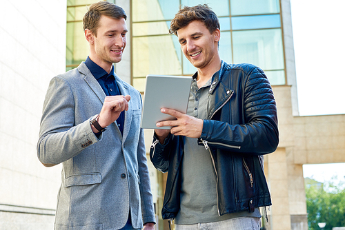 Portrait of two handsome young men using digital tablet standing outside of modern office building