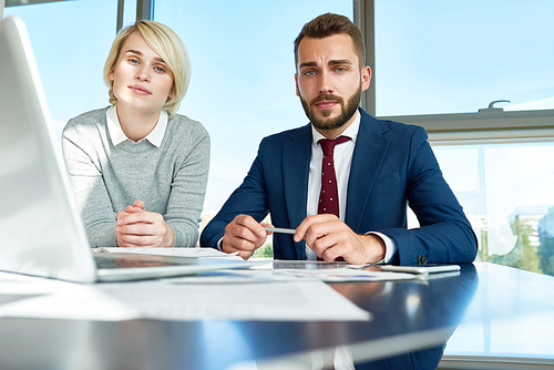 Portrait of handsome businessman and young woman  during meeting while discussing work using laptop at conference table in modern office against window