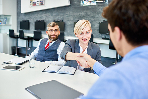 Portrait of young successful businesswoman shaking hands with partners at meeting table in board room