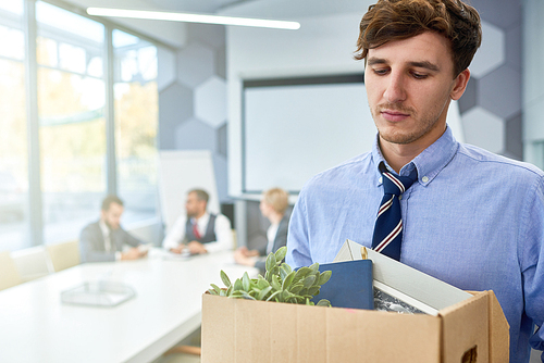 Portrait of sad young man holding box of personal belongings  fired from work in business company, copy space