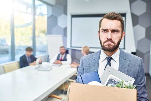 Portrait of sad bearded businessman holding box of personal belongings being fired from work in company, copy space