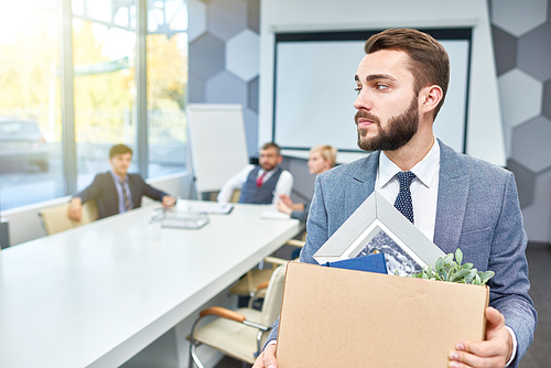 Portrait of sad bearded businessman holding box of personal belongings being fired from work, copy space