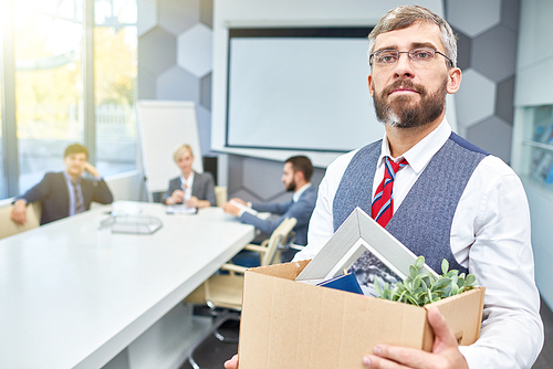 Portrait of mature bearded businessman holding box of personal belongings being fired from work in company, copy space