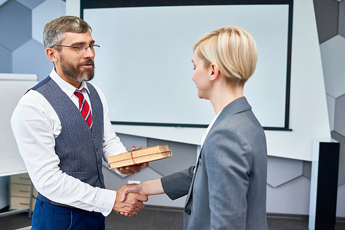 Portrait of bearded businessman shaking hands with female colleague presenting her gift for Boxing Day