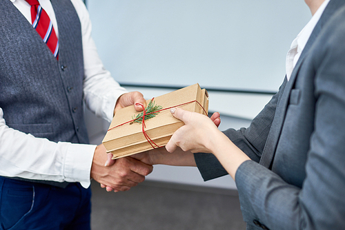 Close up view of unrecognizable businessman shaking hands with female colleague presenting her gift for Boxing Day