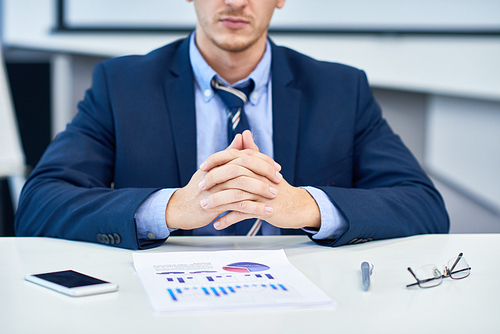 Mid-section portrait of unrecognizable business analyst sitting at desk in office with hands clasped looking at data graph