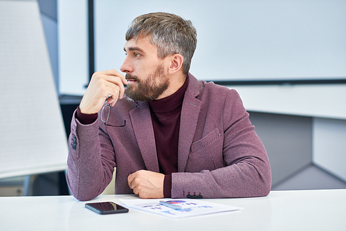 Profile view portrait of elegant mature man with greyish hair  sitting at meeting table in office listening to work discussion