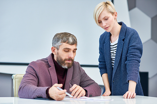 Handsome middle-aged designer and his pretty colleague brainstorming on ambitious project while having working meeting at boardroom