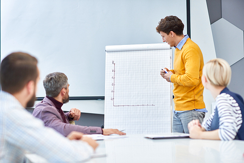 Portrait of young businessman standing at whiteboard drawing graph during marketing and research meeting in board room