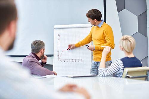 Portrait of young businessman standing at whiteboard drawing graph during marketing meeting in board room