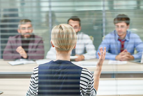 Back view of unrecognizable manager sitting opposite male colleagues and presenting her point of view concerning start-up project, view through glass wall